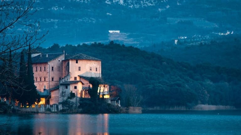 Foto di Castel Toblino, a picco sul lago con montagne dietro ad incorniciare