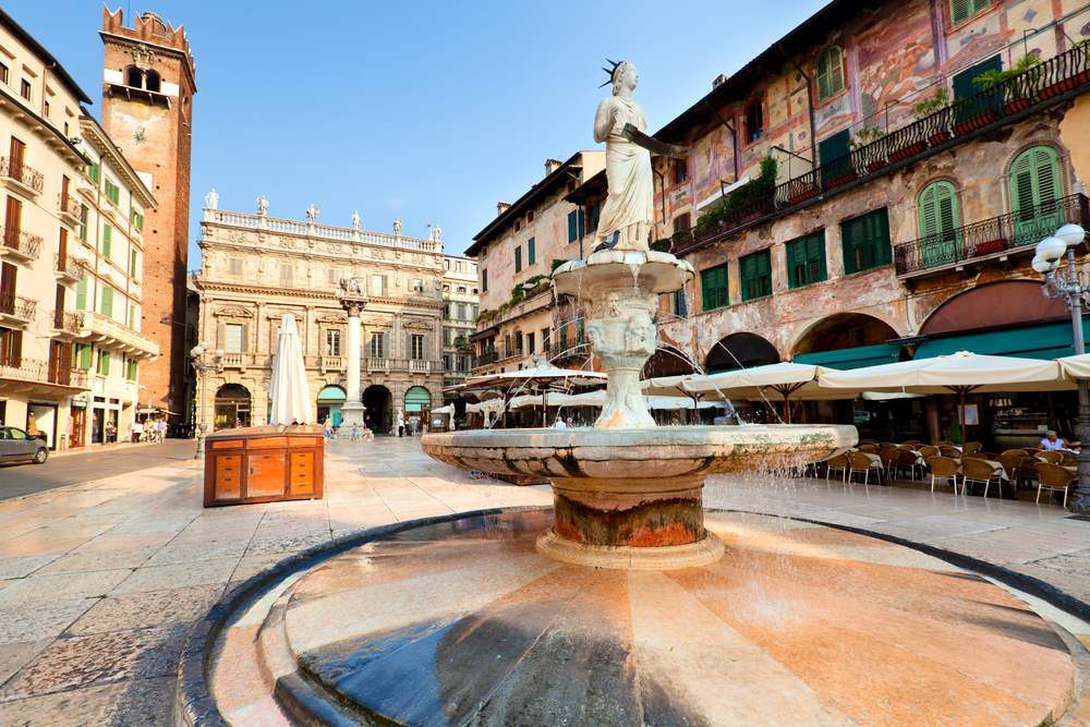 Vibrant scene of Piazza delle Erbe in Verona's heart, bustling with market stalls and framed by historical buildings under a clear sky